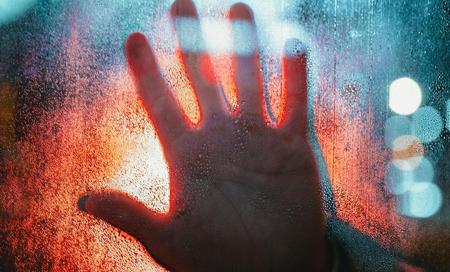 En utsträckt hand mot en färgad glasruta i motljus