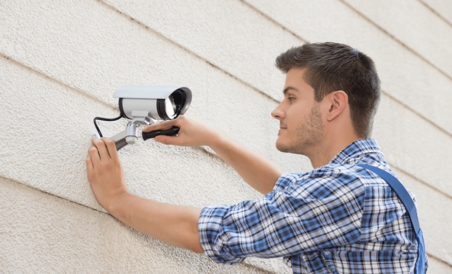 Man som skruvar upp säkerhetskamera på en vägg.